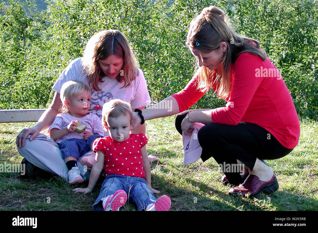 Middlefield, CT USA. Sep 2016. Young toddler holding her unfinished apple looking with curiosity about the woman stranger touching her sister`s hair. Stock Photo